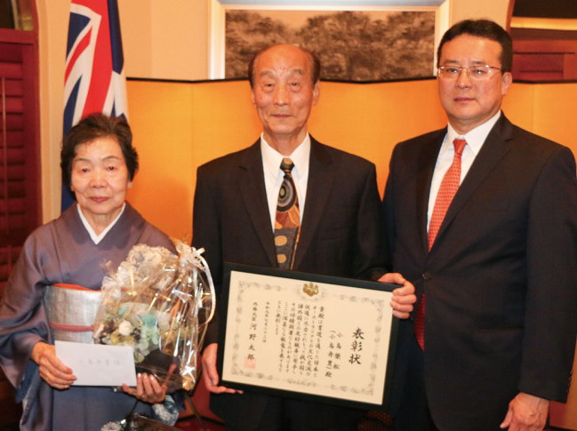 田中一成・ブリスベン総領事(右)より表彰状を受け取った小島氏(中央)と妻・文子さん(同左)(Photo:Taka Uematsu)