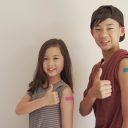 Mixed Asian young girl and teen boy giving thumb up and showing their arms with blue bandage after got vaccinated or  inoculation, child immunization, covid delta vaccine concept