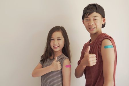 Mixed Asian young girl and teen boy giving thumb up and showing their arms with blue bandage after got vaccinated or  inoculation, child immunization, covid delta vaccine concept